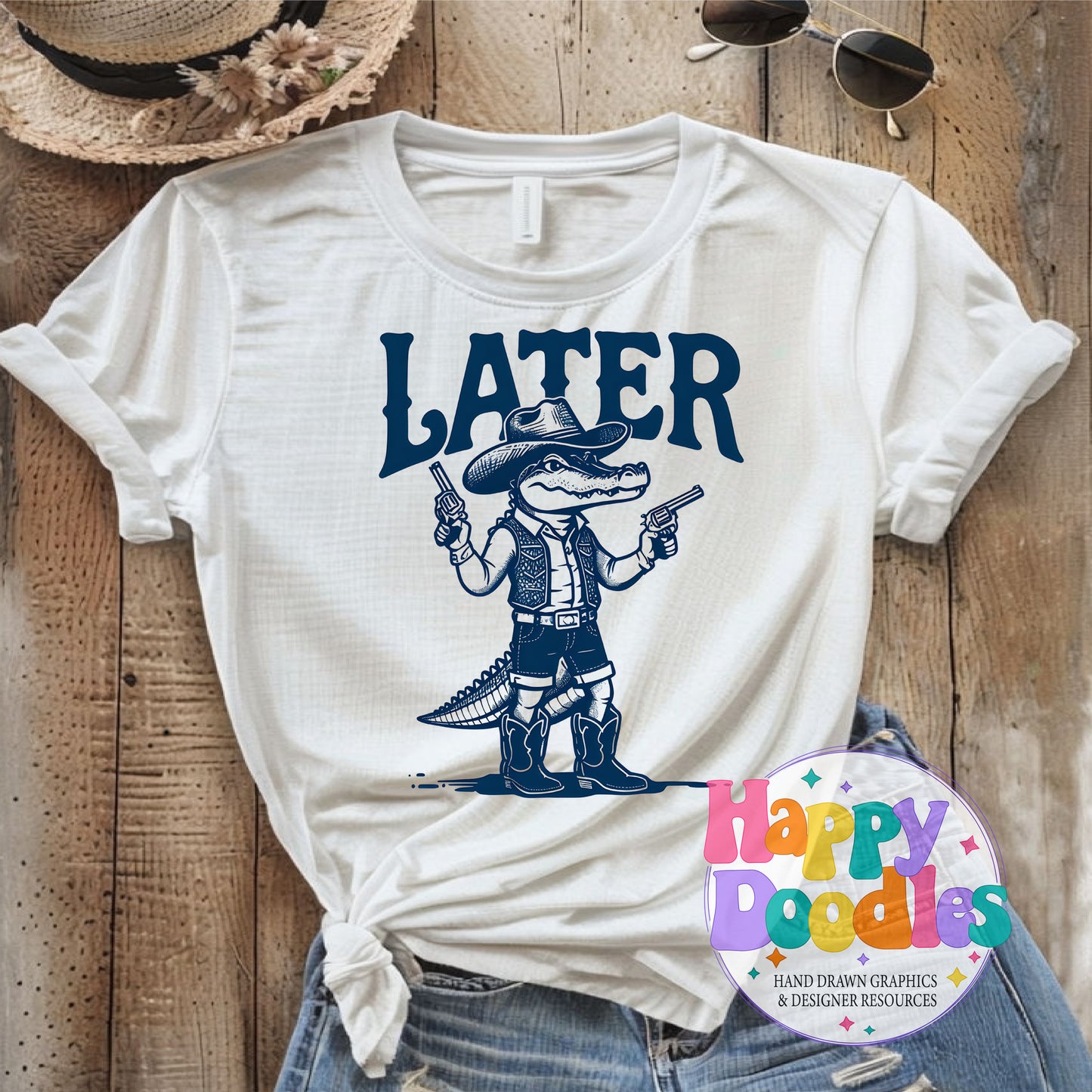 White t-shirt with a graphic of a cowboy alligator holding guns and the word 'LATER' on a wooden surface.